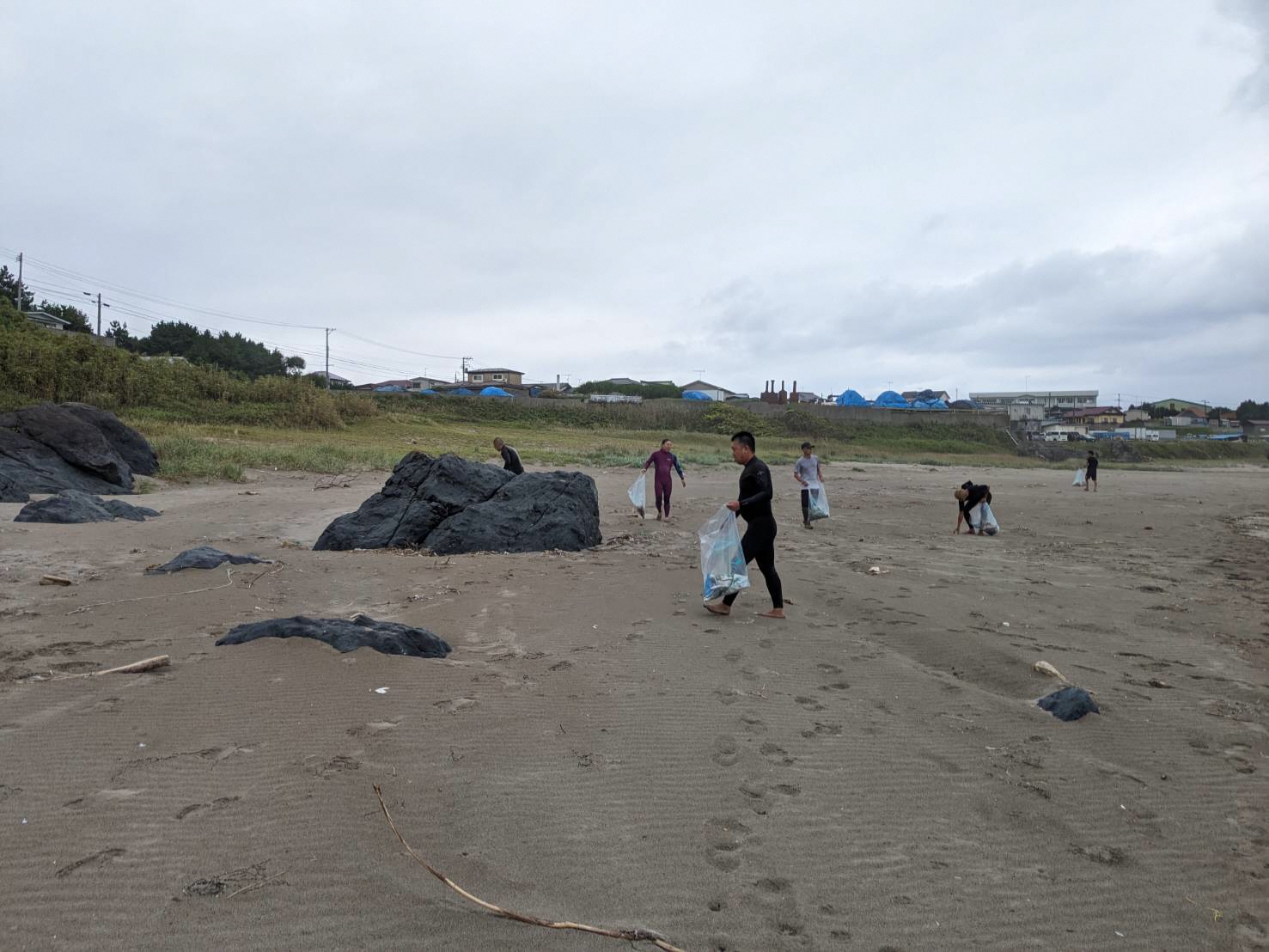 砂浜でごみを集めるサーファーの方たちの写真