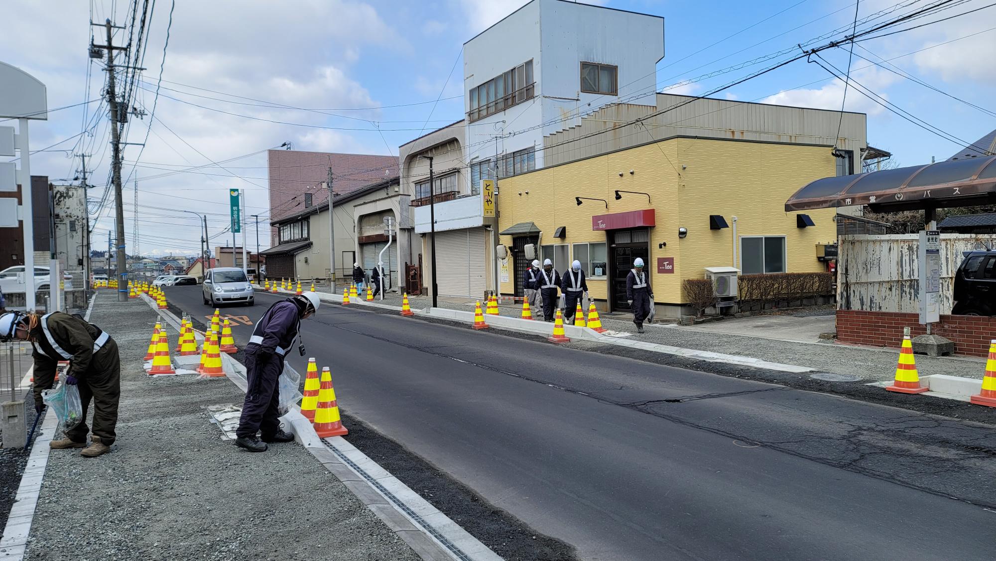 作業服ヘルメット姿で歩道のごみを拾っている写真