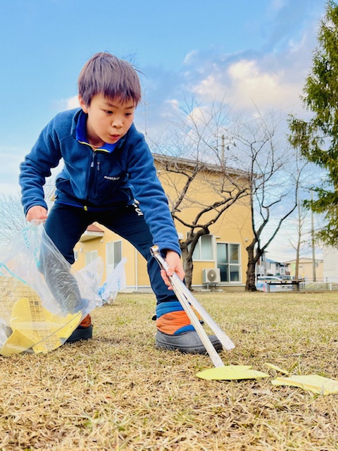 公園内のバラバラになったポリバケツの破片を拾う男児