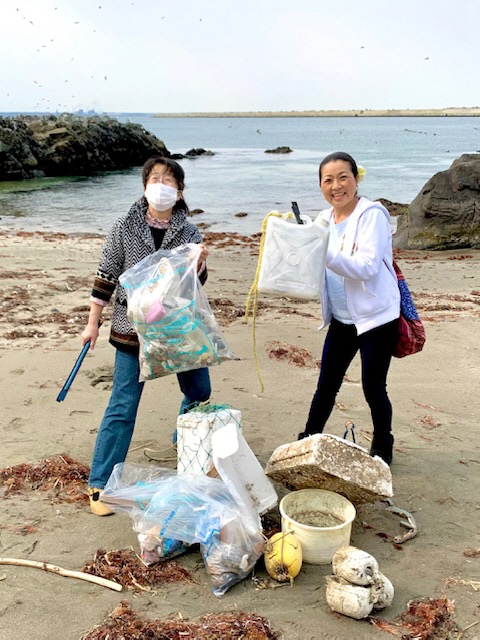 海をバックに集めたたくさんのごみと女性二人の写真