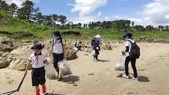 砂浜でトングとごみ袋を手にごみを拾うメンバー5名