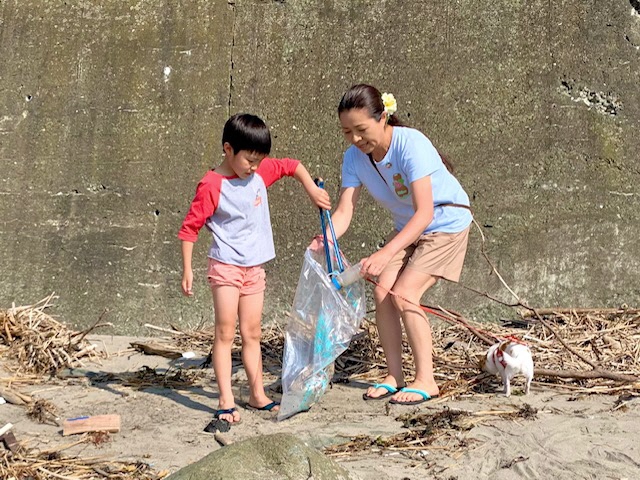 子どもがトングで拾ったごみを、ごみ袋の口を広げ持ち手伝う女性の様子