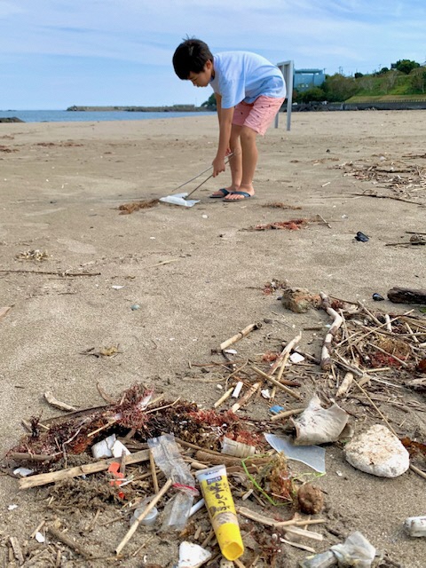 砂浜のビニール袋をトングで拾う少年