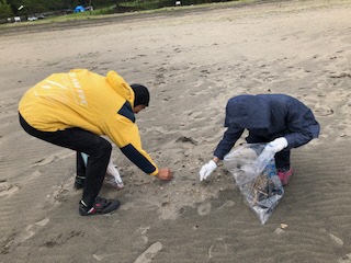 海水浴場の砂の中から、細かいごみを手で拾う男性二人