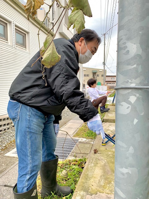 歩道になる電信柱の下のごみをトングで拾う男性の写真