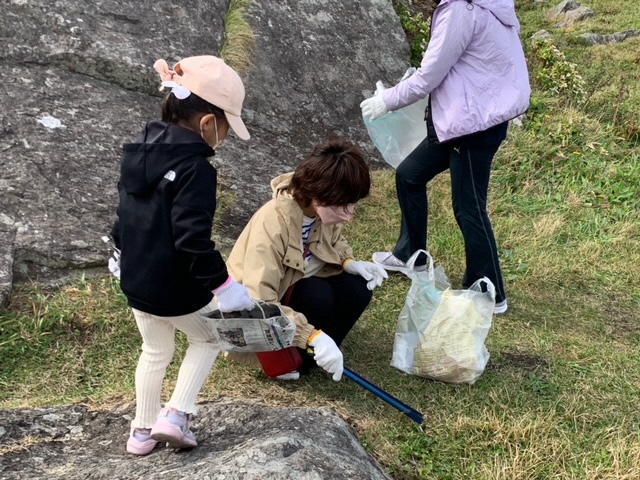 大きな岩の前の芝生地のごみを拾っている女性と子供の写真