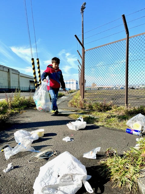 フェンス脇に散乱している、たくさんのレジ袋入りごみを拾っている子供の写真