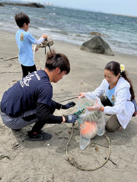 青い海をバックに、砂浜で漁の浮き玉や縄を三人で拾っている写真