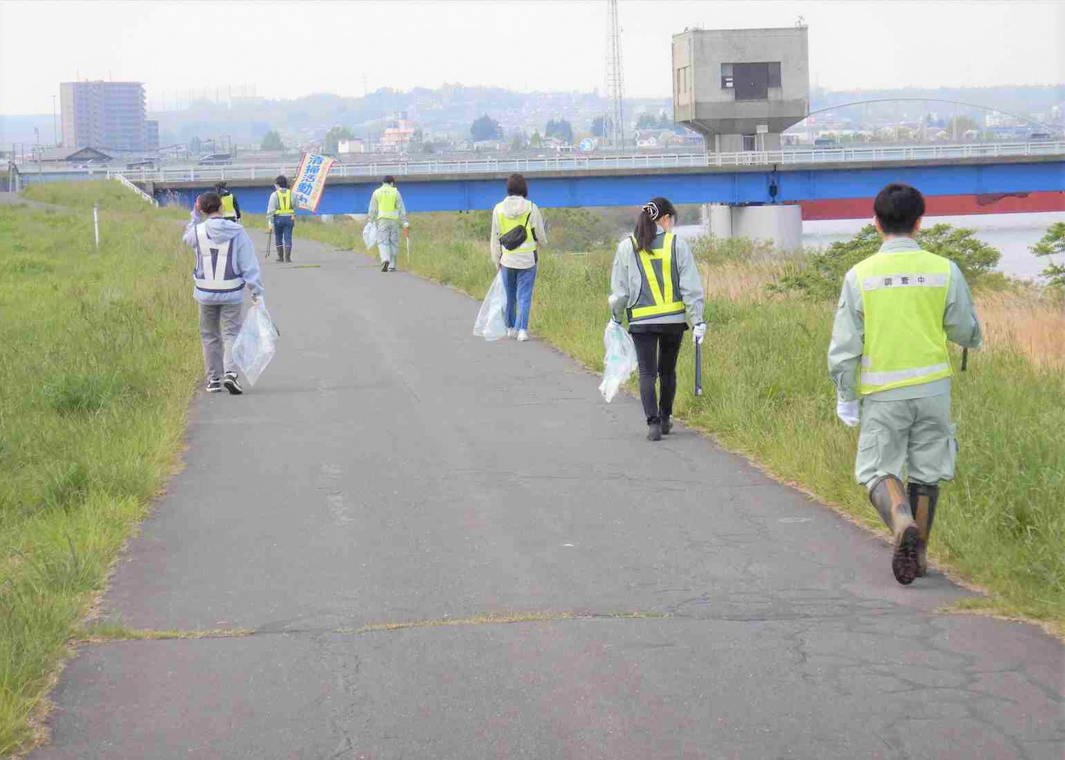 橋の見える道路のごみを拾っている六名の写真