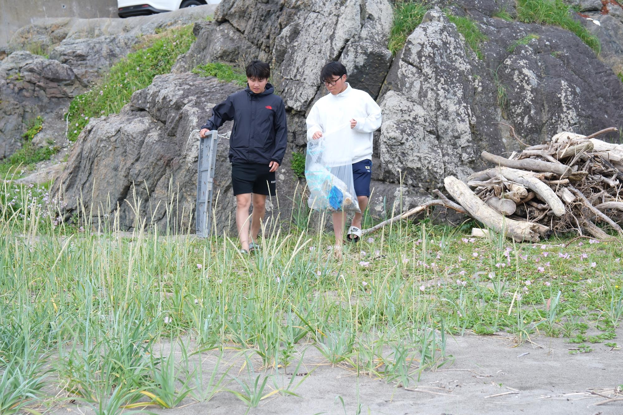 大きな岩の隣でごみを回収する二人の写真