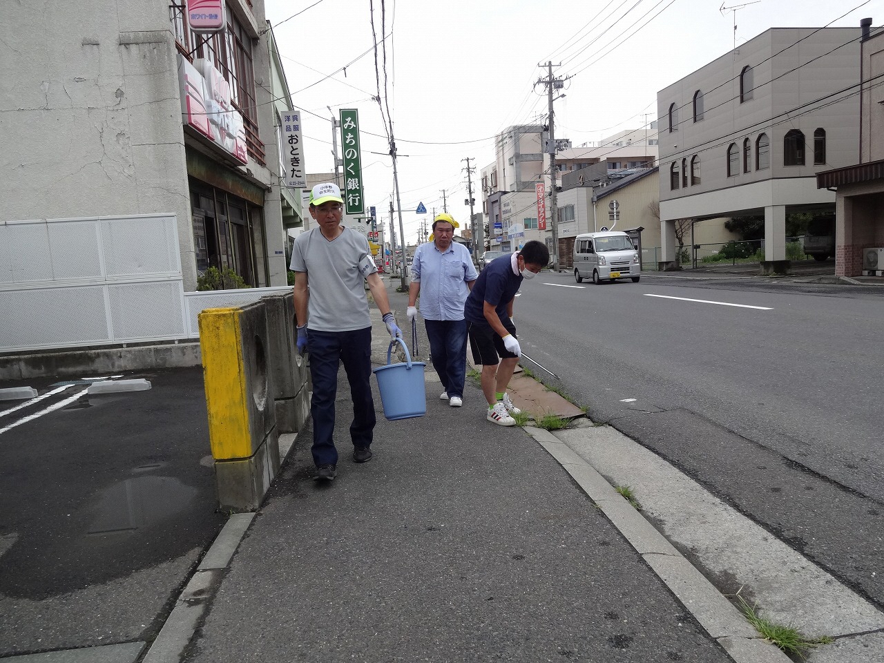 銀行の看板の見える歩道を三人でごみを拾っている写真