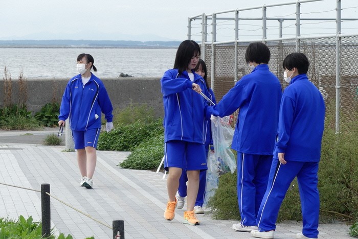 海をバックにトレーニングウエアでごみを拾う5人の生徒の写真