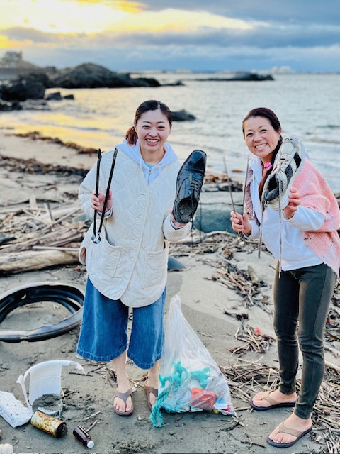 砂浜で拾った大きなくつを持っている二人の女性の写真