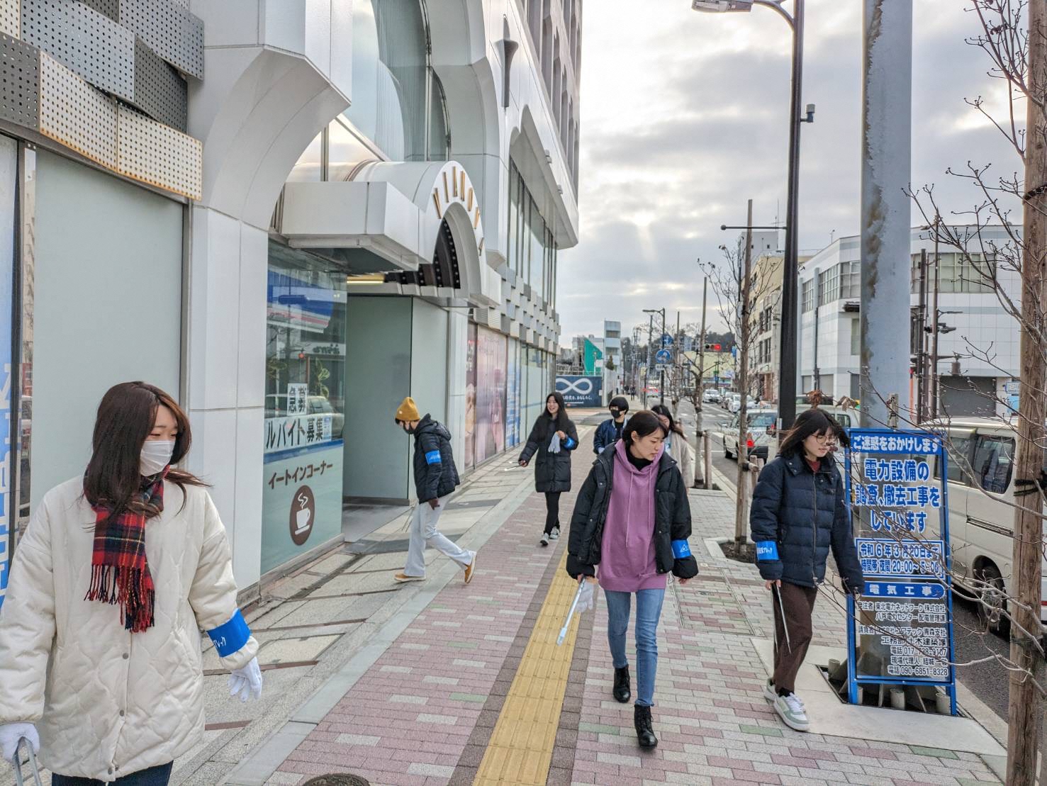 中心街のビルの前で、腕章をつけてごみを拾う人たちの写真