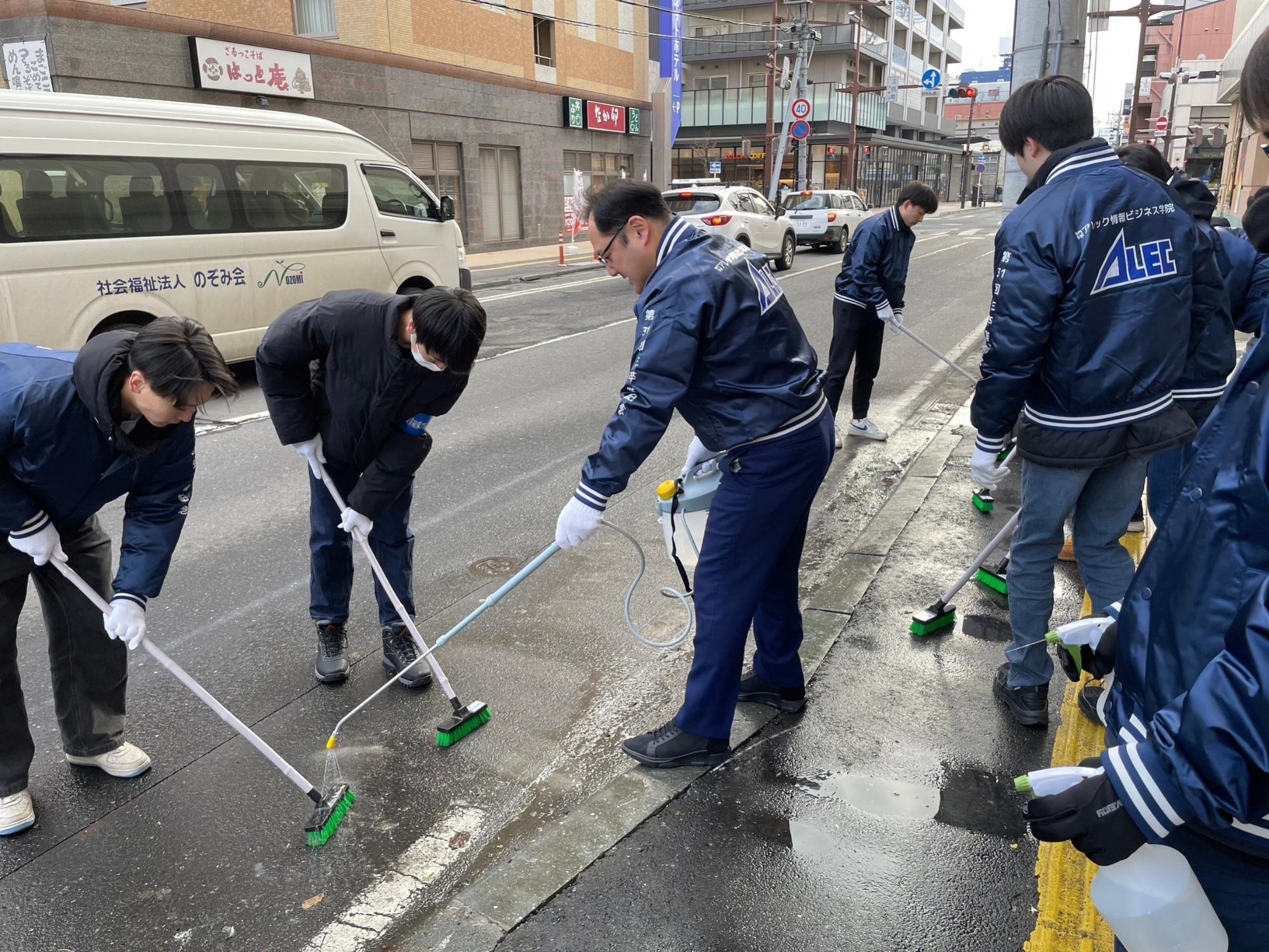 道路の鳥のフンを水を流して、デッキブラシでこすっている数名の写真