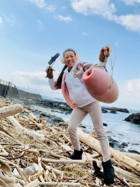 漁の浮きらしきものを拾ってこちらに見せている写真。足元は流れ着いた枝が散乱している。