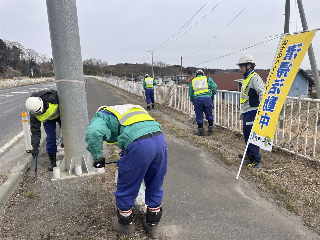 清掃活動中ののぼりを掲げて、歩道の道路標識の下のごみを拾っている写真