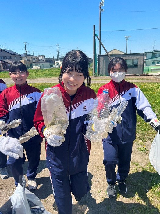 汚れたペットボトルを回収し両手に持っている生徒の写真