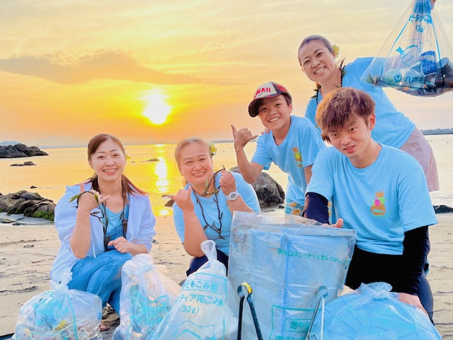 海沈む夕日をバックに回収したごみを持ち集合写真