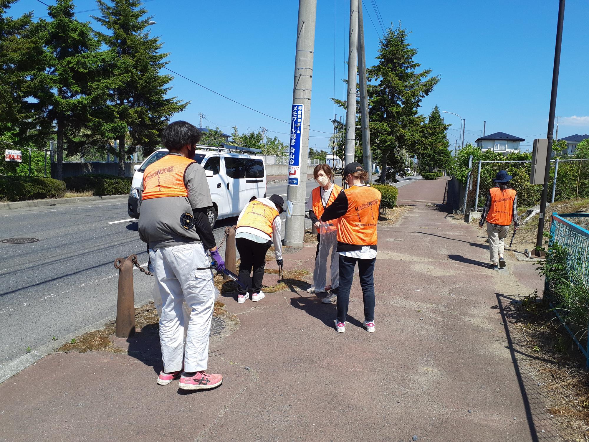 オレンジ色のビブスを着用し、歩道のごみを拾っている5人の写真
