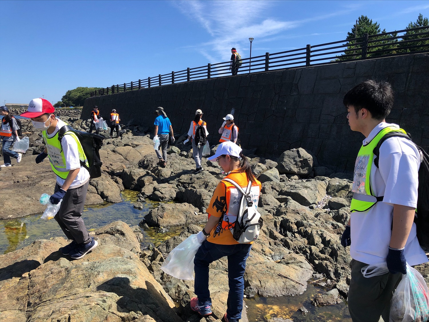 道路下の岩場でビブスを着用し、活動する人たちの写真