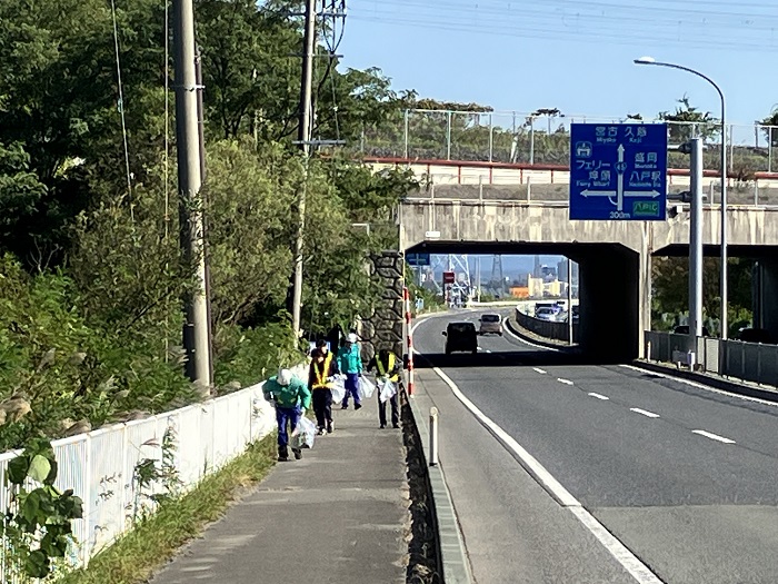 北インターバイパス歩道と車道の引きの写真。歩道を作業服の参加者が手にごみ袋を持って活動している。