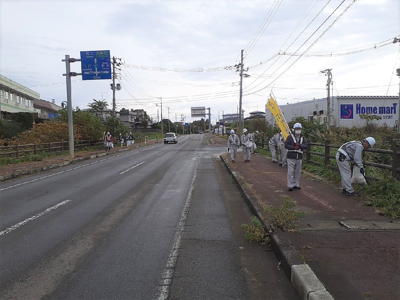 道路脇の歩道のごみを集めている参加者の写真。作業服、ヘルメット、安全帯を着用している。