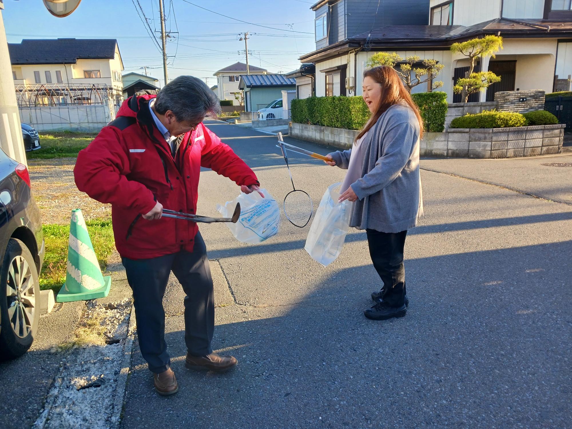 石堂の住宅地。拾った草刈り鎌とバドミントンのラケットを持っている参加者の写真。