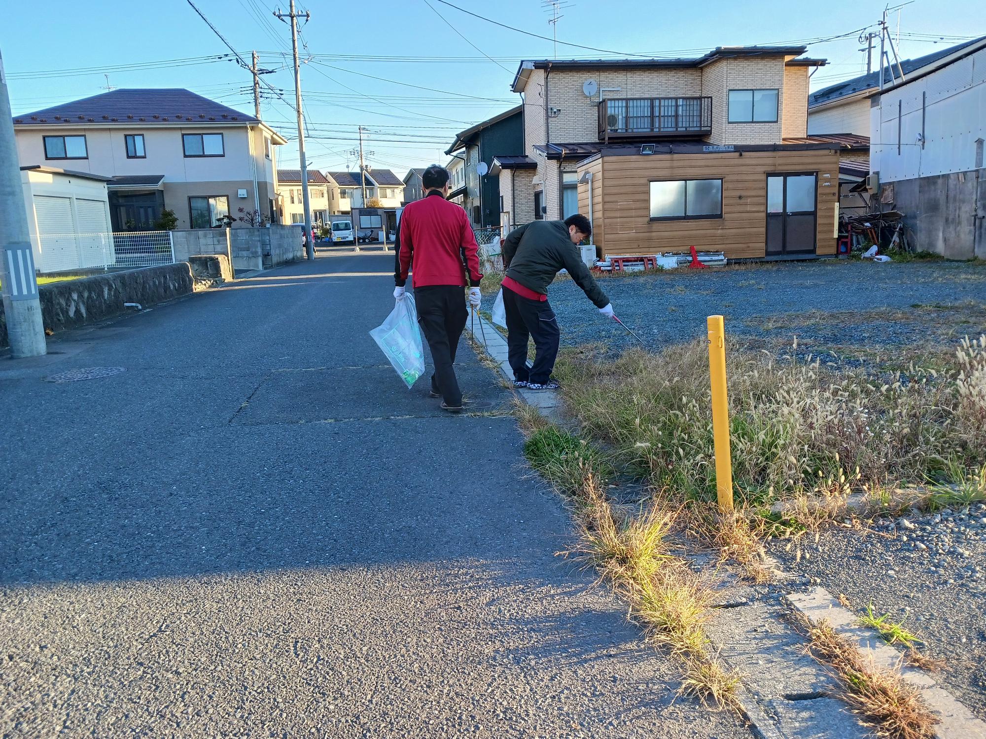 石堂の住宅地。道路脇の雑草付近でごみを拾う参加者の写真。