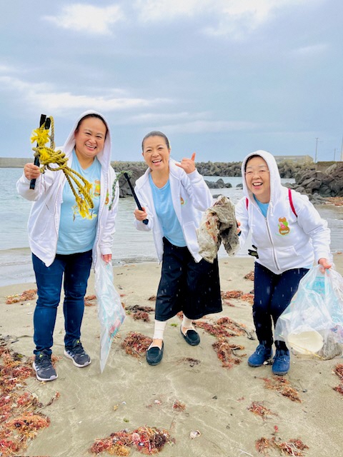砂浜でトングで拾った縄などを掲げている女性三人の写真。