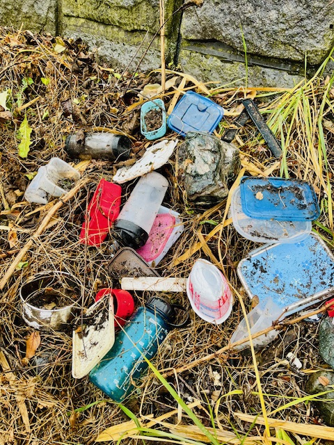 雑草の上にあるプラスチック容器などのごみの写真。