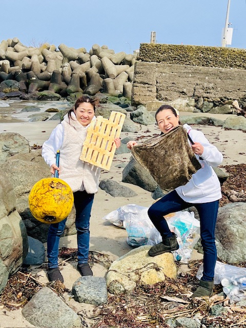 青空の海岸。二人の女性が集めた浮き玉等を見せている写真。