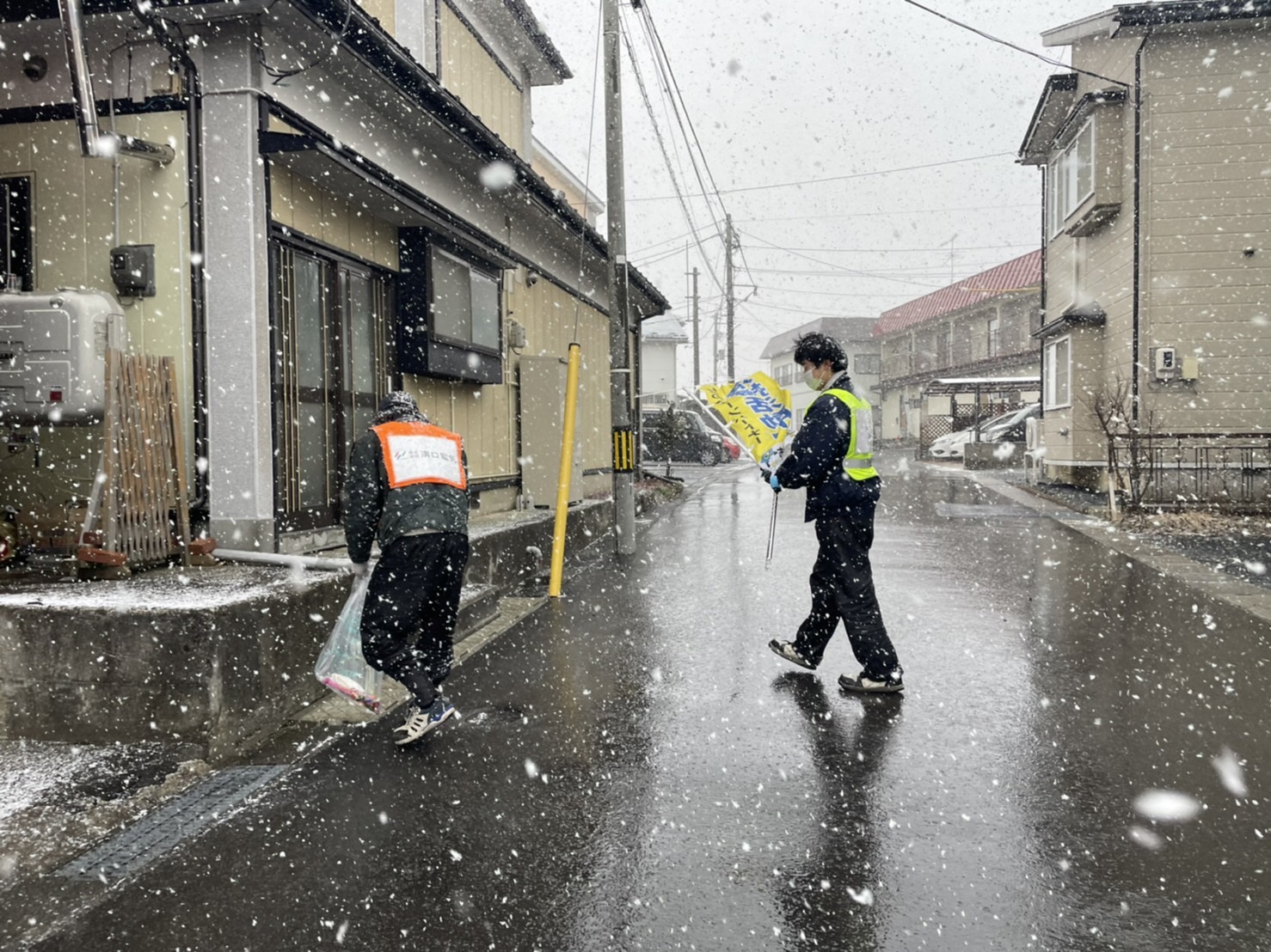 雪が舞う中住宅街のごみを拾う写真