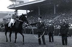競馬場での騎手の長吉とクリフジと背広を着た男性3人との優勝の記念写真
