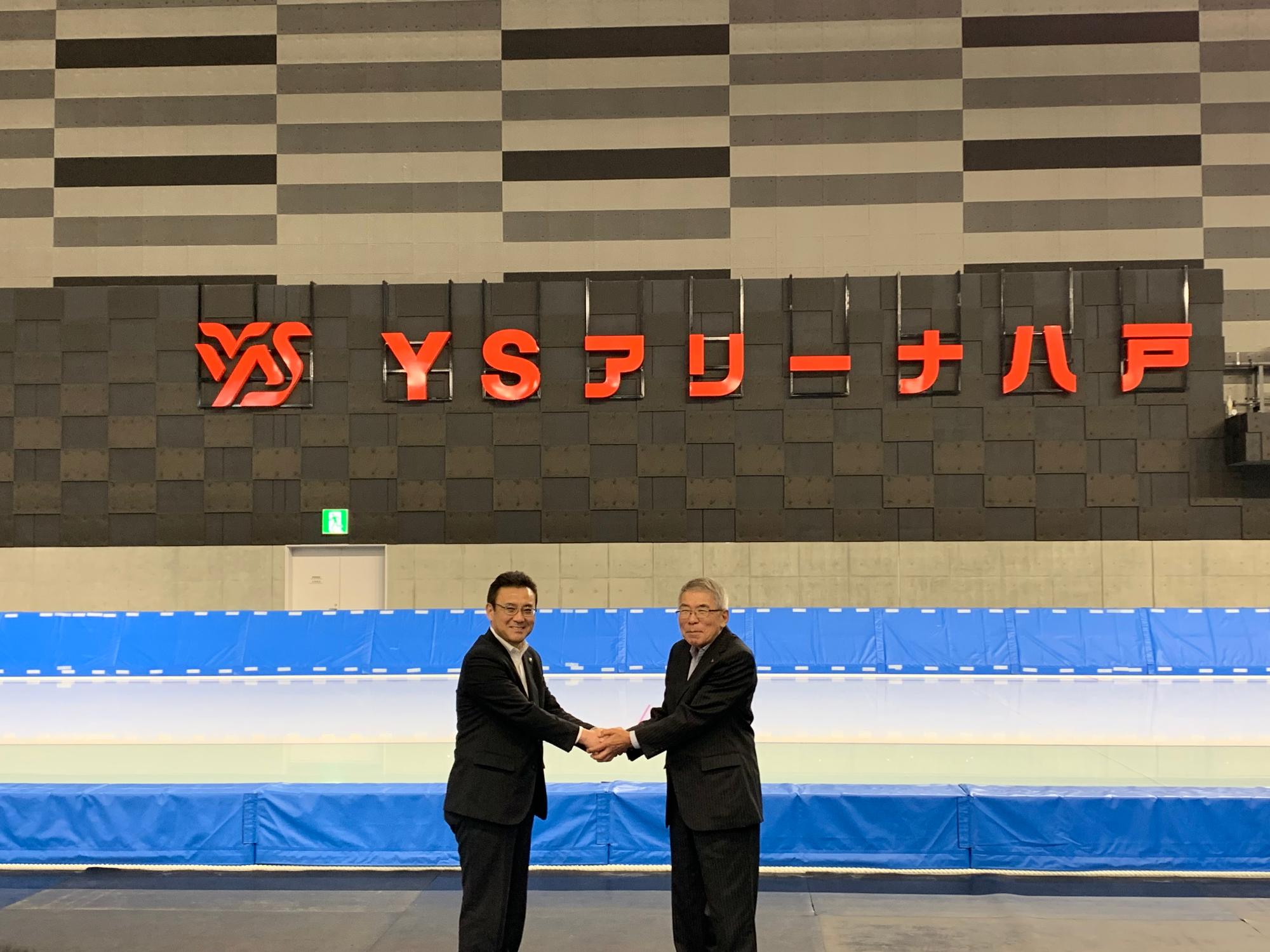 吉田社長と八戸市長がYSアリーナ八戸の特定呼称を背景に握手している写真