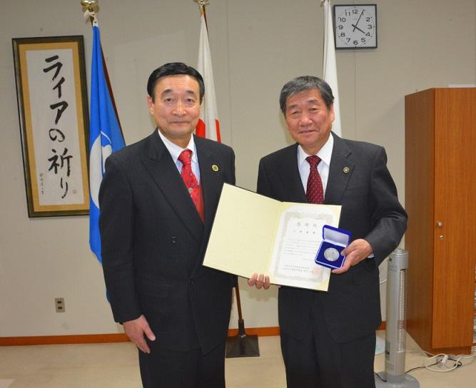 野田 公俊教授と感謝状と記念のメダルを持ち記念撮影をしている市長の写真