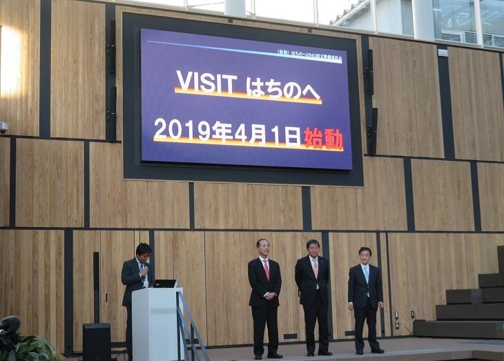 VISITはちのへ2019年4月1日始動と映し出されたスクリーンと司会者・八戸市物産協会、八戸観光コンベンション協会の代表、市長が舞台上に並んでいる写真