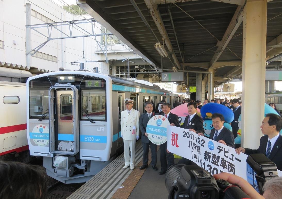 駅構内で八戸線の新型車両「キハE130系500代」の前市長・関係者・キャラクター達が集まり記念撮影をしている写真