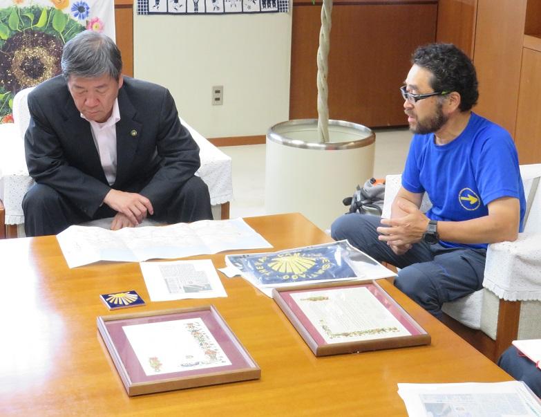 机の上に置かれている資料に目を向け、高橋 晃氏と会談している市長の写真