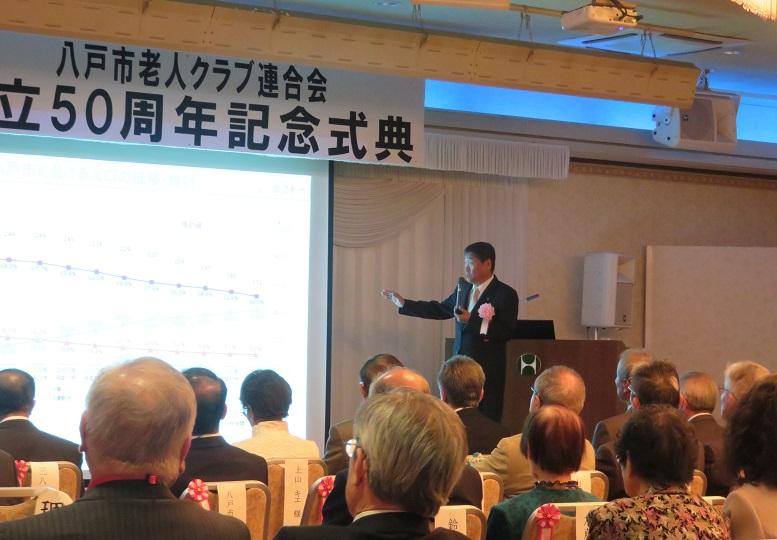 八戸市老連創立50周年記念式典祝賀会でスクリーンを見ながら説明をしている市長の写真