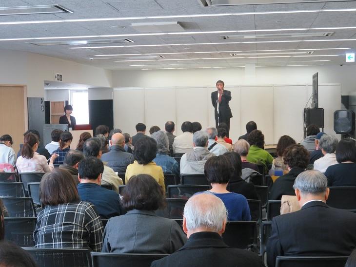 八戸市の新しい美術館を考えるシンポジウム会場で挨拶をしている市長の話しを聞いている参加者の後ろ姿の写真