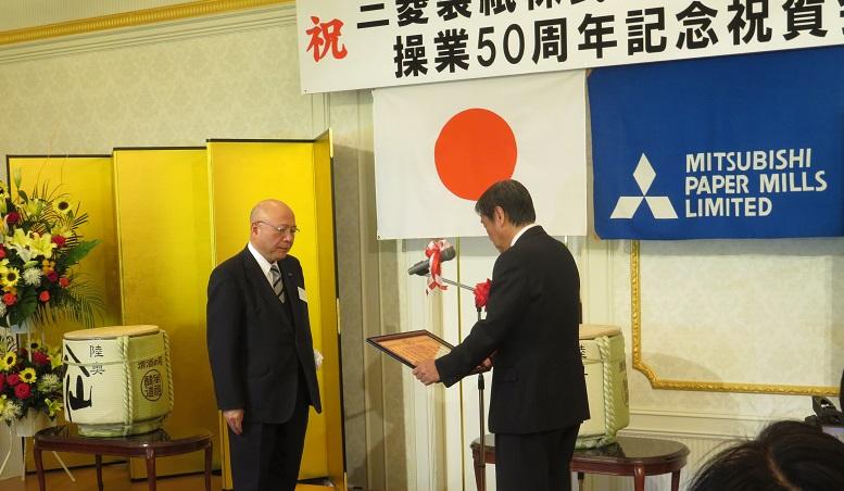 三菱製紙株式会社八戸工場操業50周年記念祝賀会で額縁に入った感謝状を両手に持ち贈呈している市長の写真