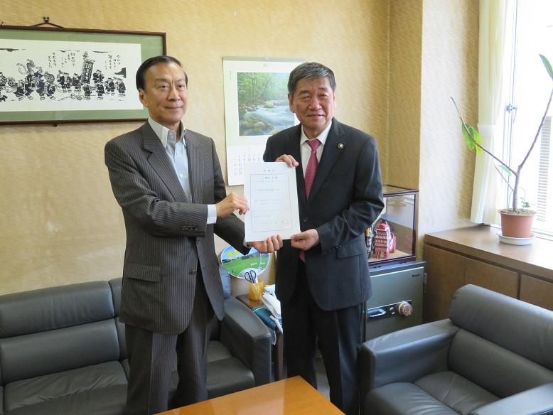 市東京事務所内で柳谷理事長と市長が2人で交付状を持っている記念写真