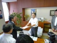 市長室で市政評価委員会代表者の男性が市長に書類を手渡している写真