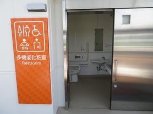 トイレの入り口左側に男女共同、車いす利用者、障がい者、赤ちゃんが一緒でも利用可能な絵文字表示のある多目的トイレの写真