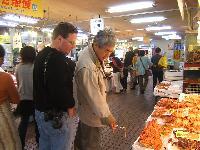 八食センターで揚げ物売り場で食品の説明を受けているフェデラルウェイ市長の写真