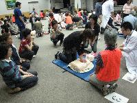 AED講習会で上半身の人形を用いて救命の練習を行う女性と指導員の写真