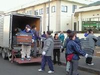 中型のトラックの荷台から物資を運び出している6人ほどの男女の写真
