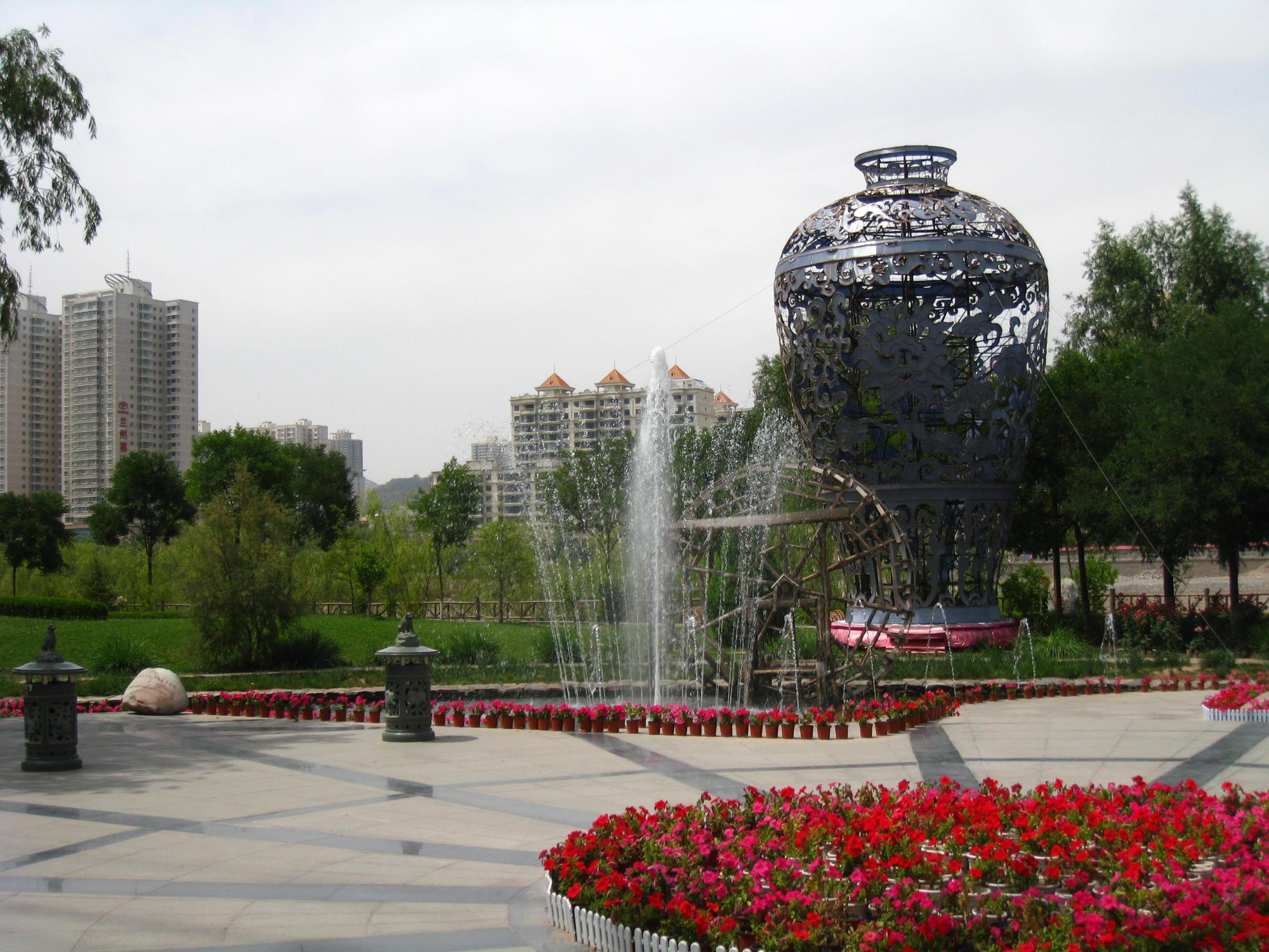 噴水と赤い花と大きな花瓶のアートが印象的な公園の写真