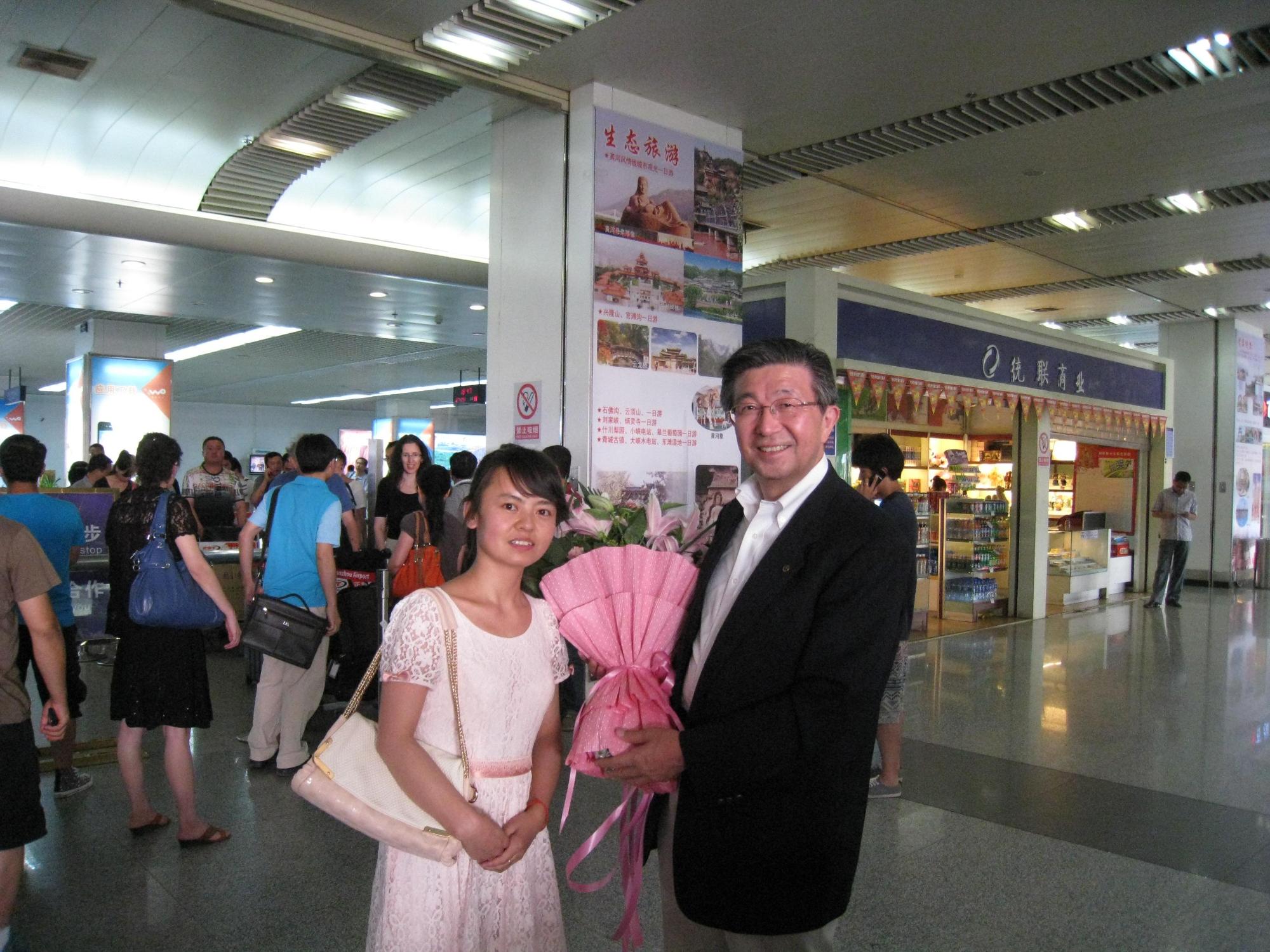 薄いピンクのワンピースを着た女学生とピンクの花束を持つスーツ姿の男性が笑顔で写っている記念写真